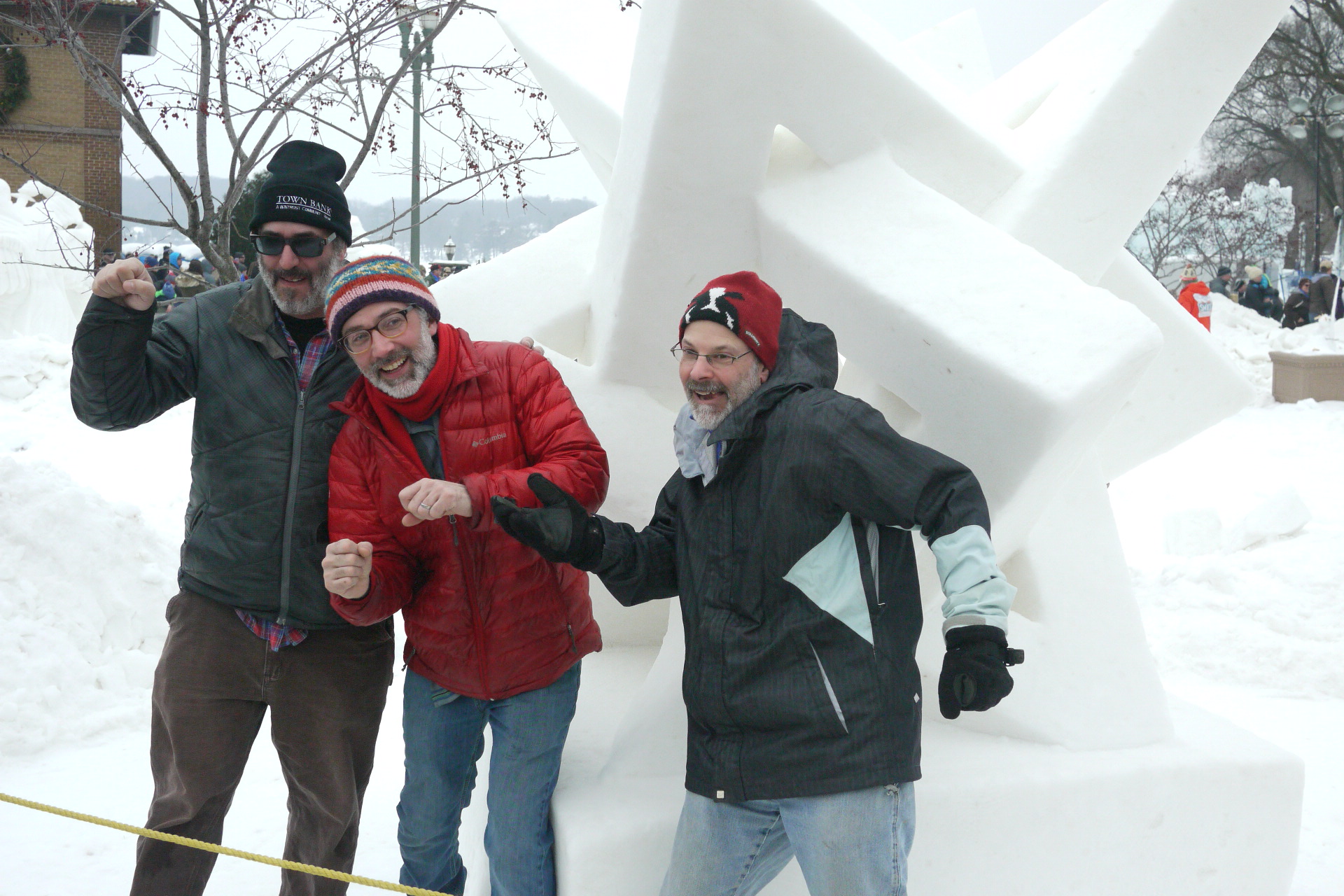 A set of very large intertwined triangles carved out of snow with the three artist standing in front with smiles and gesticulations.